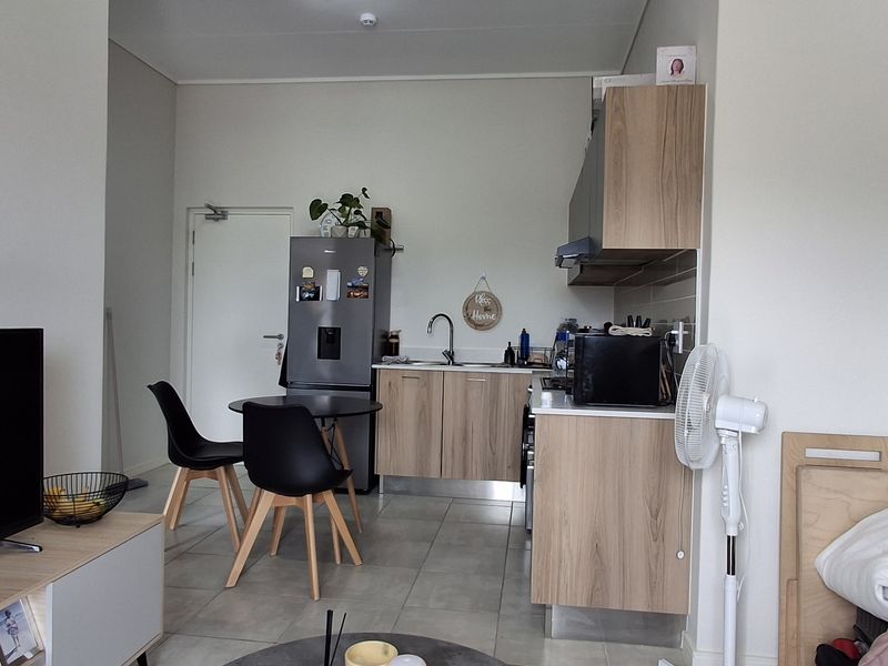Open-plan living area featuring a compact kitchen with modern wood-finish cabinetry, tiled flooring, and integrated fixtures, creating a functional and cohesive living space.