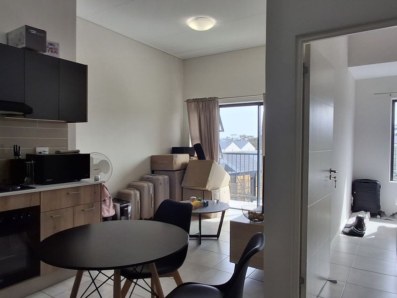 Open-plan kitchen and living area featuring modern cabinetry, built-in appliances, and tiled flooring, with direct access to a balcony and adjacent bedroom.