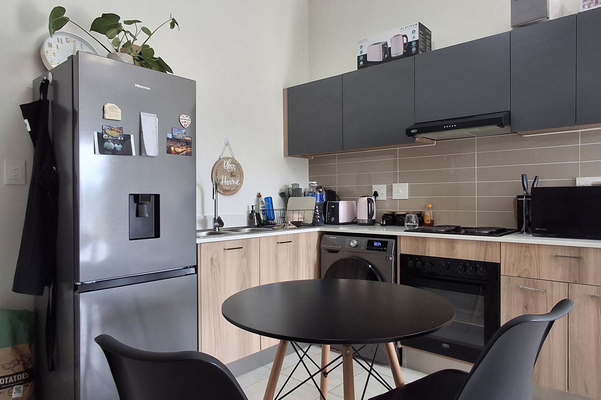 Modern kitchen featuring wood-finish lower cabinetry, dark grey upper cabinets, tiled backsplash, and integrated appliances including an oven and extractor fan.