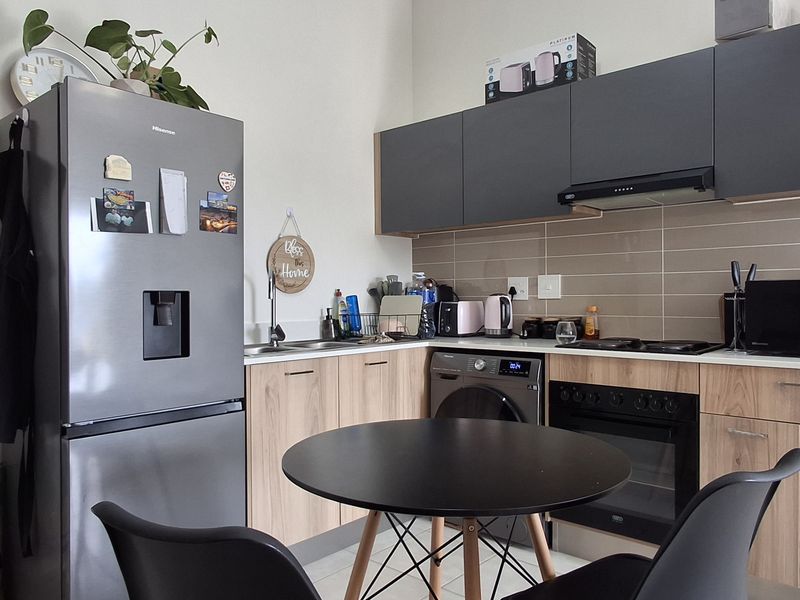 Modern kitchen featuring wood-finish lower cabinetry, dark grey upper cabinets, tiled backsplash, and integrated appliances including an oven and extractor fan.