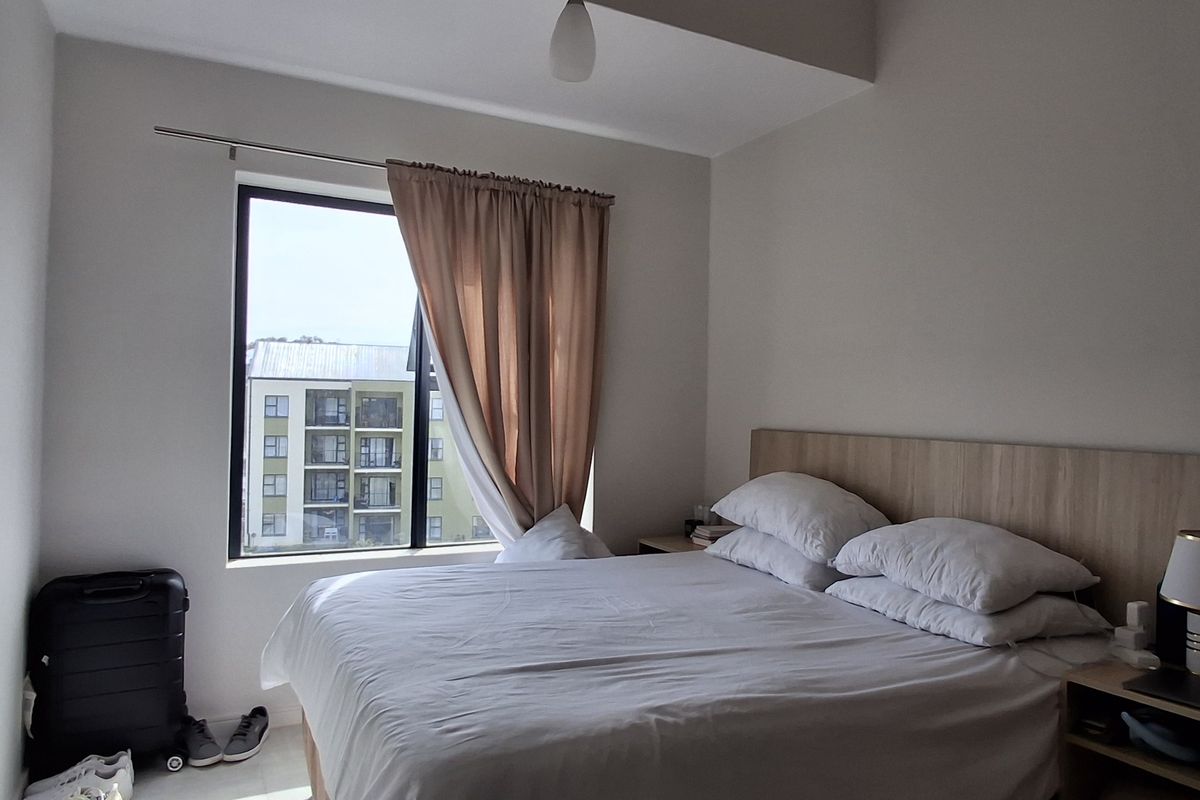 A well-lit bedroom featuring a built-in headboard and a large window providing natural light and an exterior view.