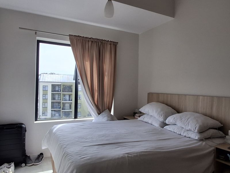 A well-lit bedroom featuring a built-in headboard and a large window providing natural light and an exterior view.
