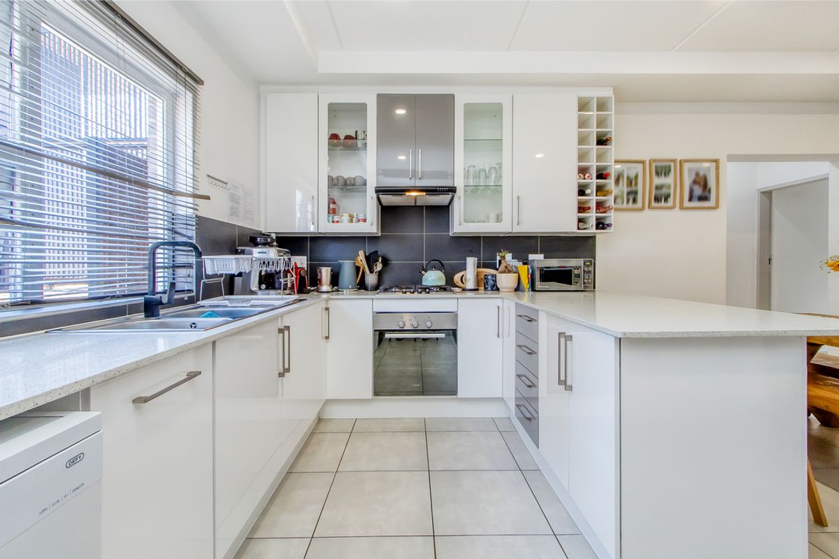 Modern kitchen featuring white cabinetry, stone countertops, integrated stainless steel appliances, tiled backsplash, and a functional U-shaped layout with ample storage.