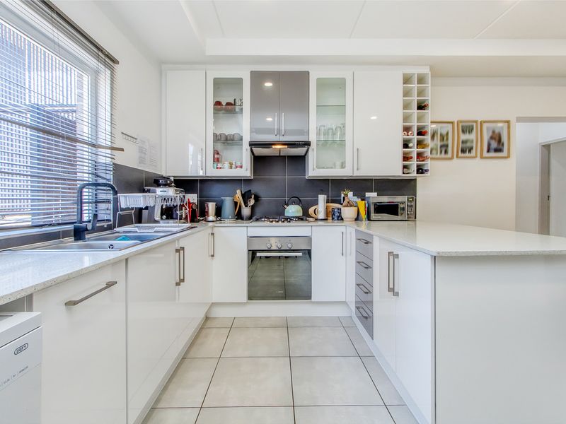 Modern kitchen featuring white cabinetry, stone countertops, integrated stainless steel appliances, tiled backsplash, and a functional U-shaped layout with ample storage.