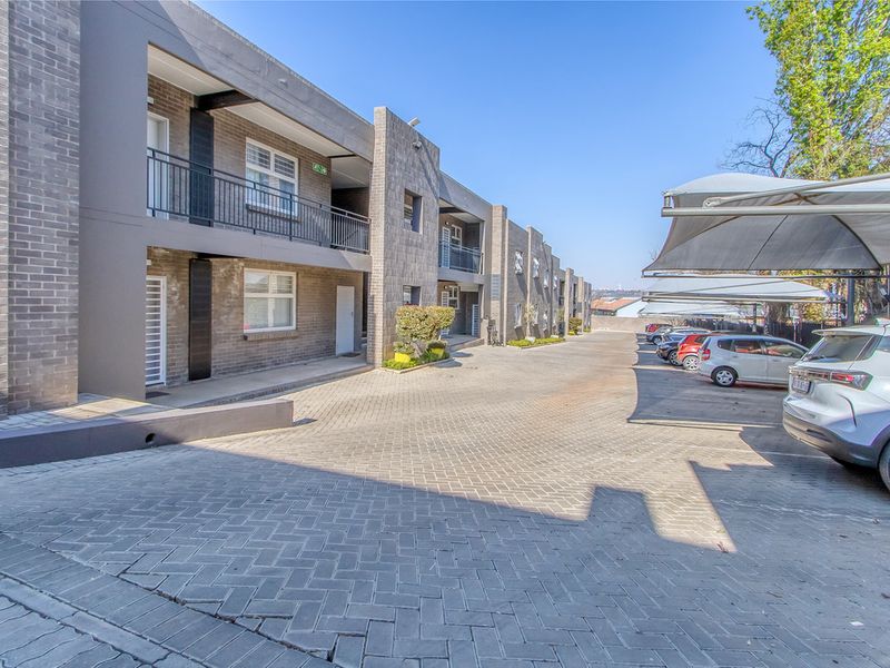 Exterior view of a modern apartment complex featuring a paved driveway, covered parking bays, and multi-level units with balconies.