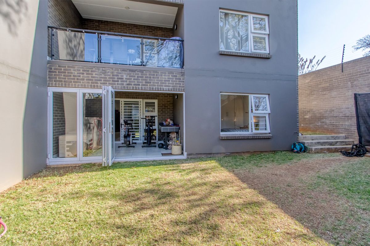 Rear view of a modern apartment building featuring a private garden, ground floor patio with folding doors, and an upper-level balcony with glass balustrades.