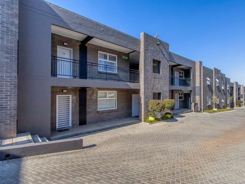 A modern multi-story apartment complex featuring a brick facade, paved driveway, and private balconies with security gates.