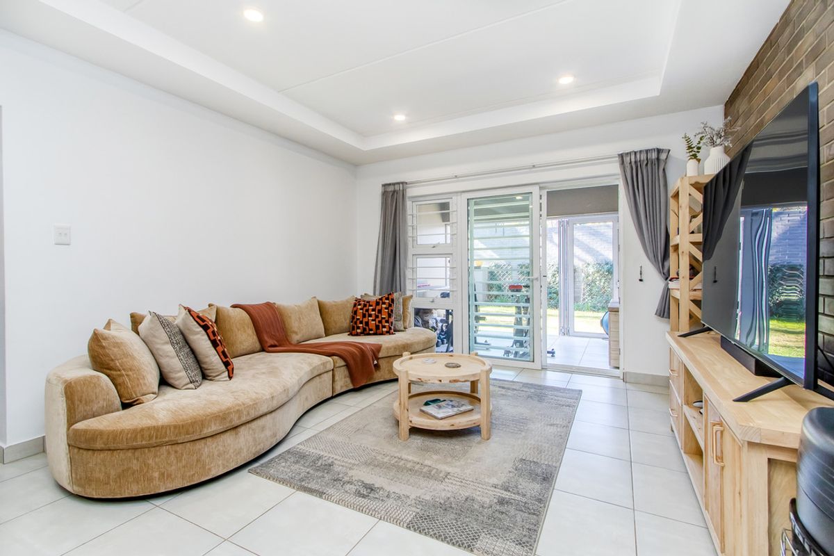 Bright living room featuring tiled flooring, a recessed ceiling with downlights, and a brick feature wall, with direct access to an outdoor patio area.