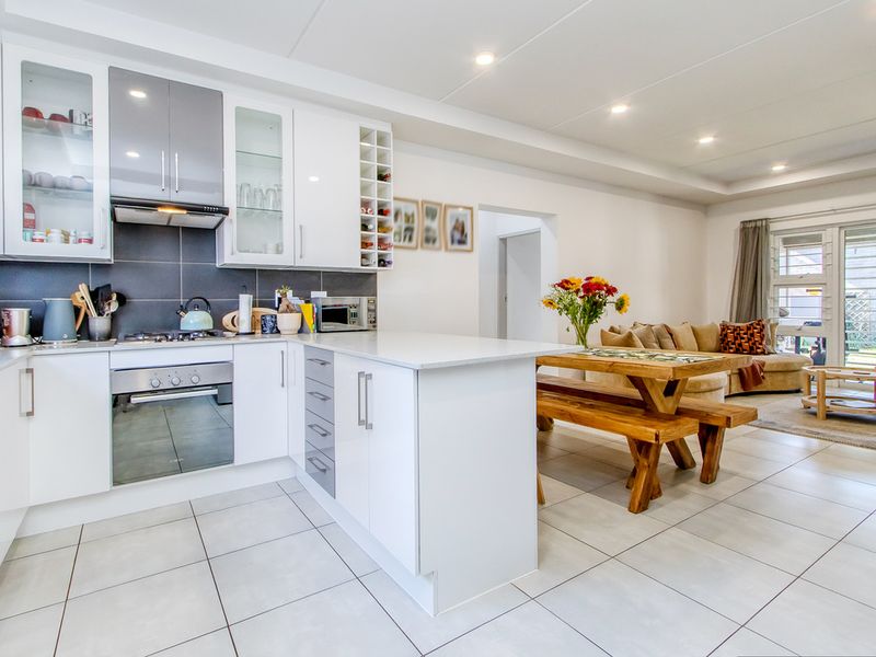 Modern open-plan kitchen and living area featuring sleek cabinetry, stone countertops, integrated appliances, and tiled flooring with direct access to an outdoor patio.
