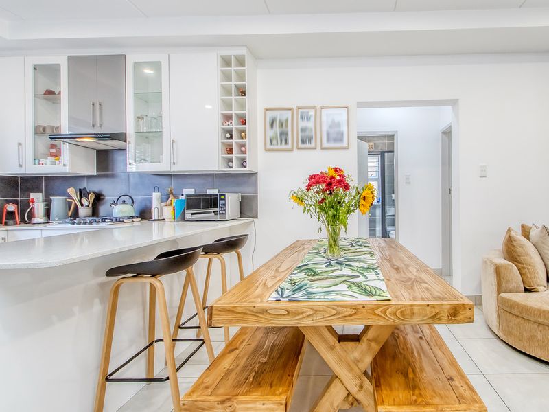 Modern open-plan kitchen and dining area featuring white cabinetry, stone countertops, integrated hob, and tiled flooring, creating a bright and functional living space.
