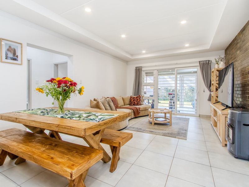 Bright open-plan living and dining area featuring tiled floors, recessed lighting, a brick feature wall, and sliding doors leading to the patio.
