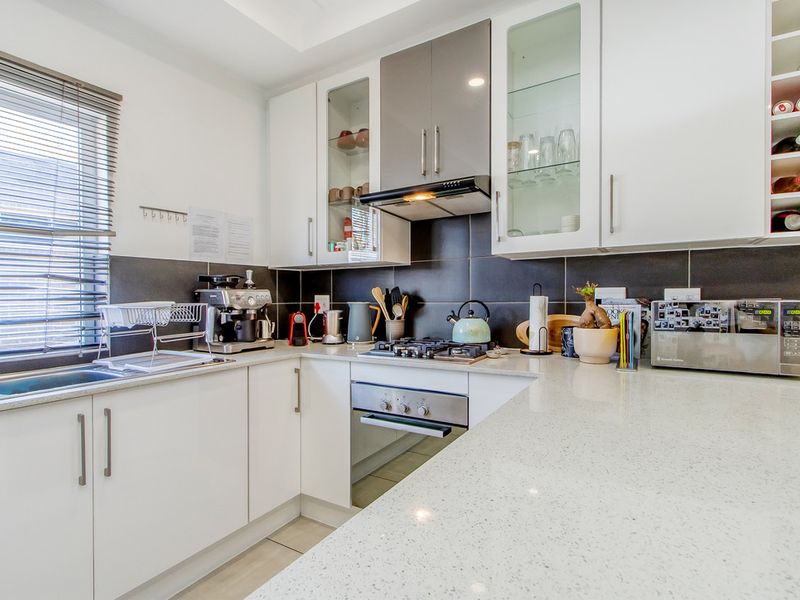 Modern kitchen featuring white cabinetry, quartz countertops, built-in oven, gas hob, extractor fan, and a dedicated wine rack.