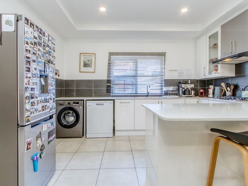 Modern kitchen featuring white cabinetry, stone countertops, tiled splashback, integrated gas hob, and recessed lighting, with dedicated space for laundry appliances.