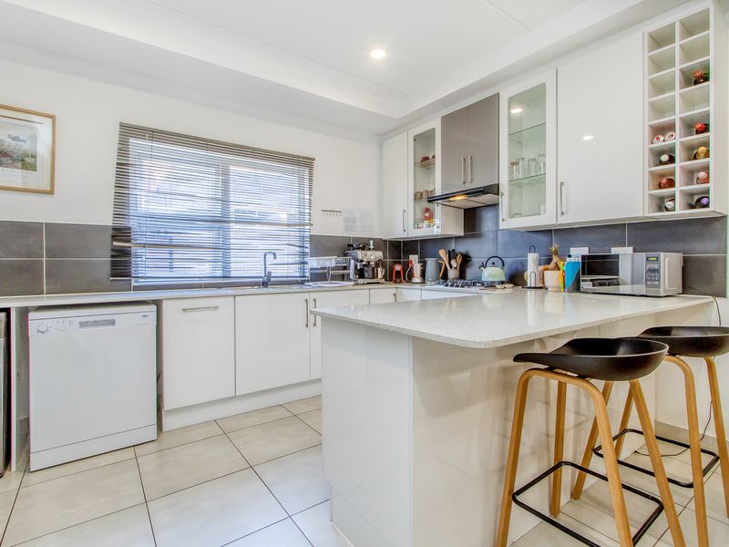 Modern kitchen featuring white cabinetry, stone countertops, tiled backsplash, integrated wine rack, and tiled flooring with ample workspace.