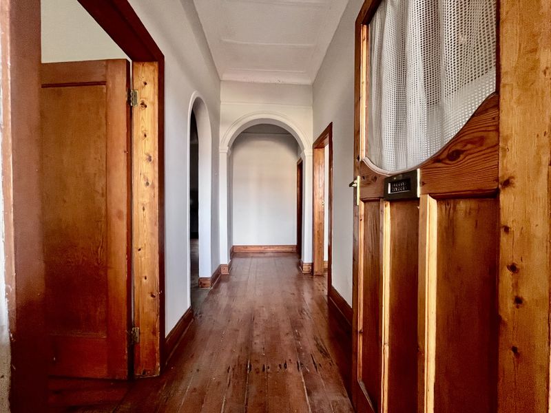 A long interior hallway featuring original timber flooring, arched architectural details, and classic wooden door frames throughout the space.