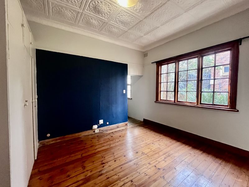 A vacant bedroom featuring original pressed metal ceilings, polished timber flooring, and built-in storage cupboards with large timber-framed windows.