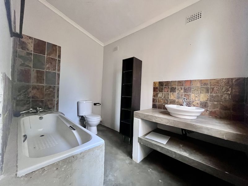 A functional bathroom featuring a built-in bathtub, a concrete vanity with a vessel sink, and stone tile accents.