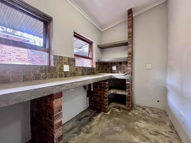 A functional scullery or utility area featuring rustic exposed brick supports, concrete countertops, built-in shelving, and tiled splashbacks.