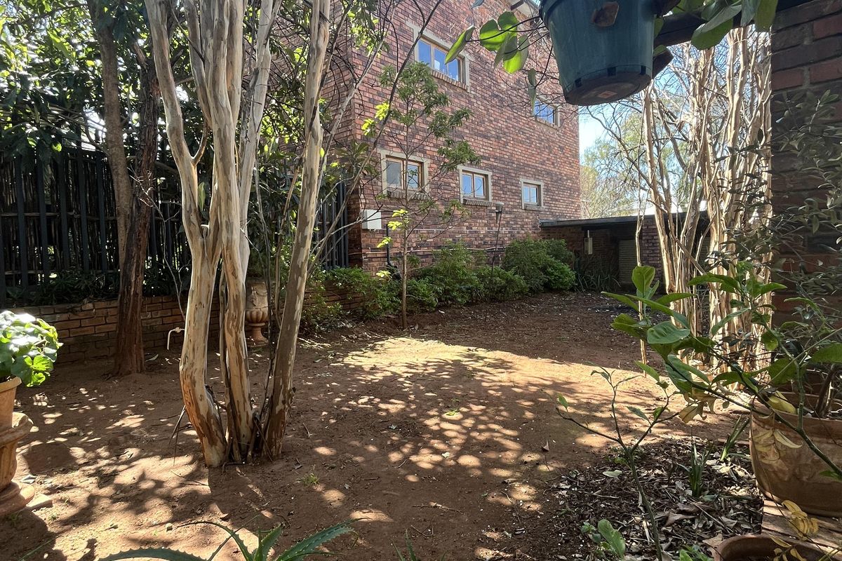 A view of the rear garden area featuring mature trees and a multi-story face brick building facade.