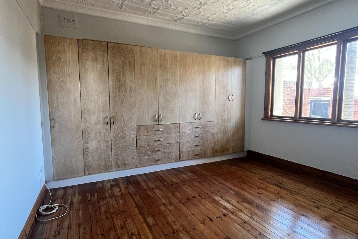 Spacious bedroom featuring original timber flooring, a decorative pressed metal ceiling, and extensive built-in timber cabinetry for storage.
