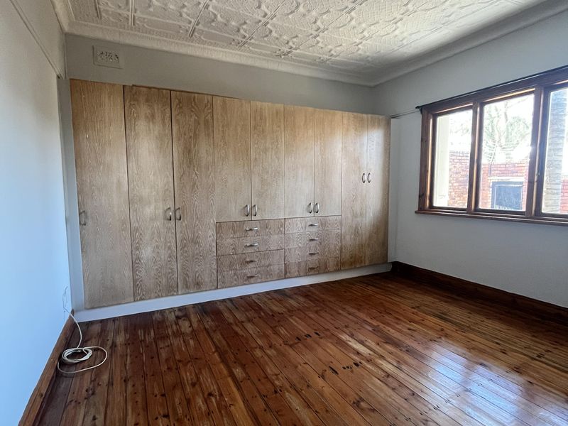 Spacious bedroom featuring original timber flooring, a decorative pressed metal ceiling, and extensive built-in timber cabinetry for storage.