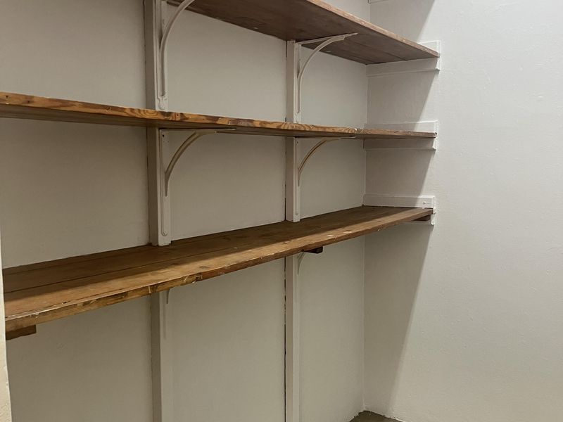 A functional utility space or pantry area featuring built-in wooden shelving units mounted on white walls with concrete flooring.