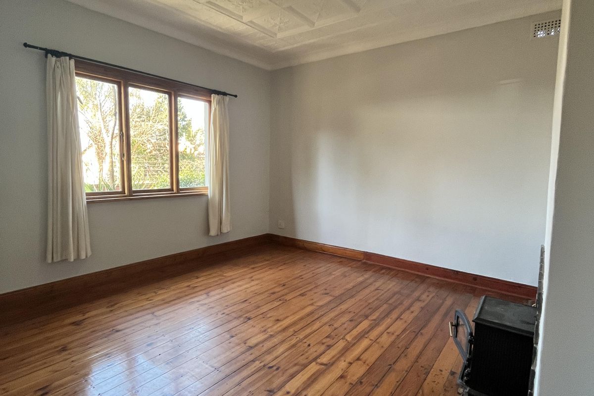 Spacious living room featuring original timber flooring, an ornate plaster ceiling with a central rose, and a built-in wood burning stove.
