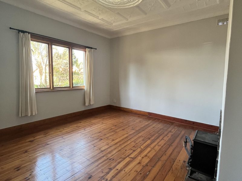 Spacious living room featuring original timber flooring, an ornate plaster ceiling with a central rose, and a built-in wood burning stove.