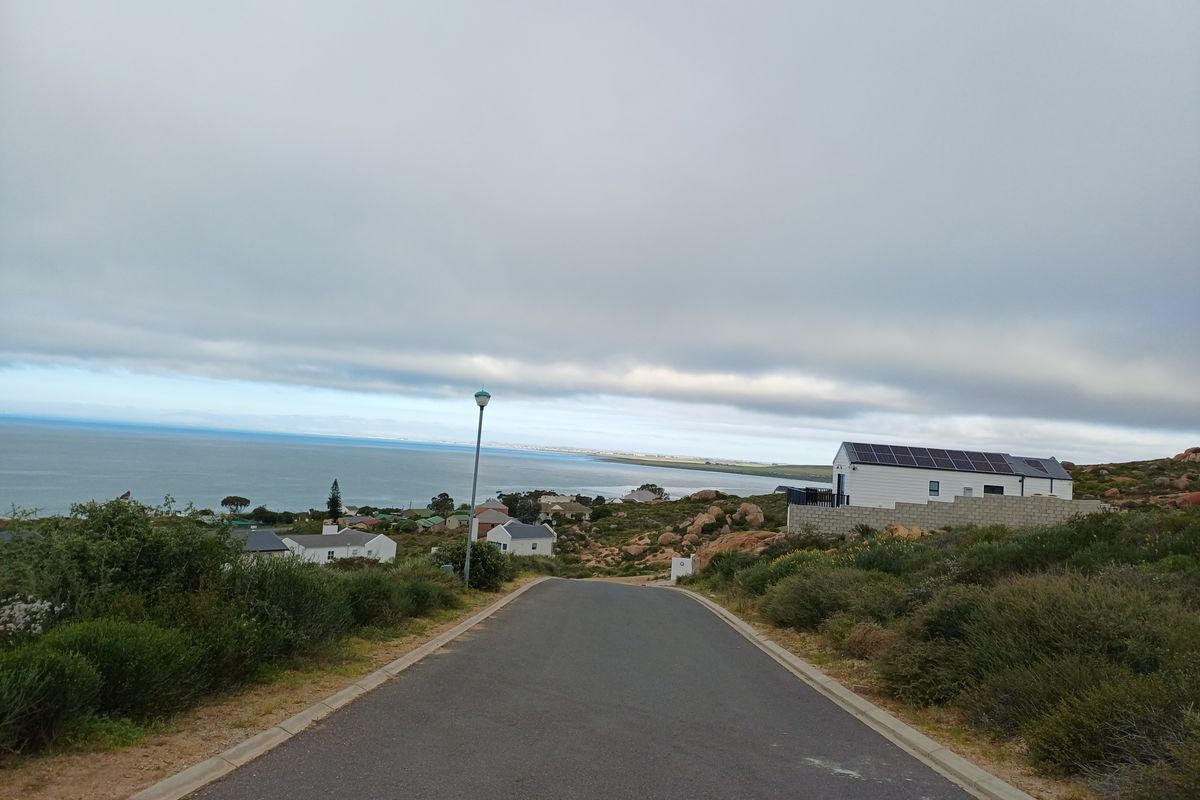 A view looking down a paved residential street towards the coastline, featuring nearby homes and clear ocean views.