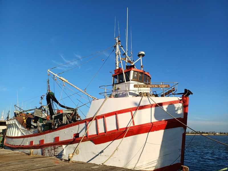 A fishing vessel docked at a pier, showing exterior hull and deck equipment.
