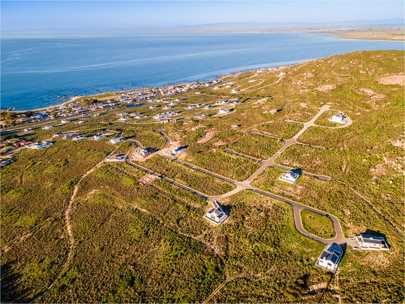 An aerial view of a coastal residential development featuring paved road infrastructure and established plots overlooking the ocean.