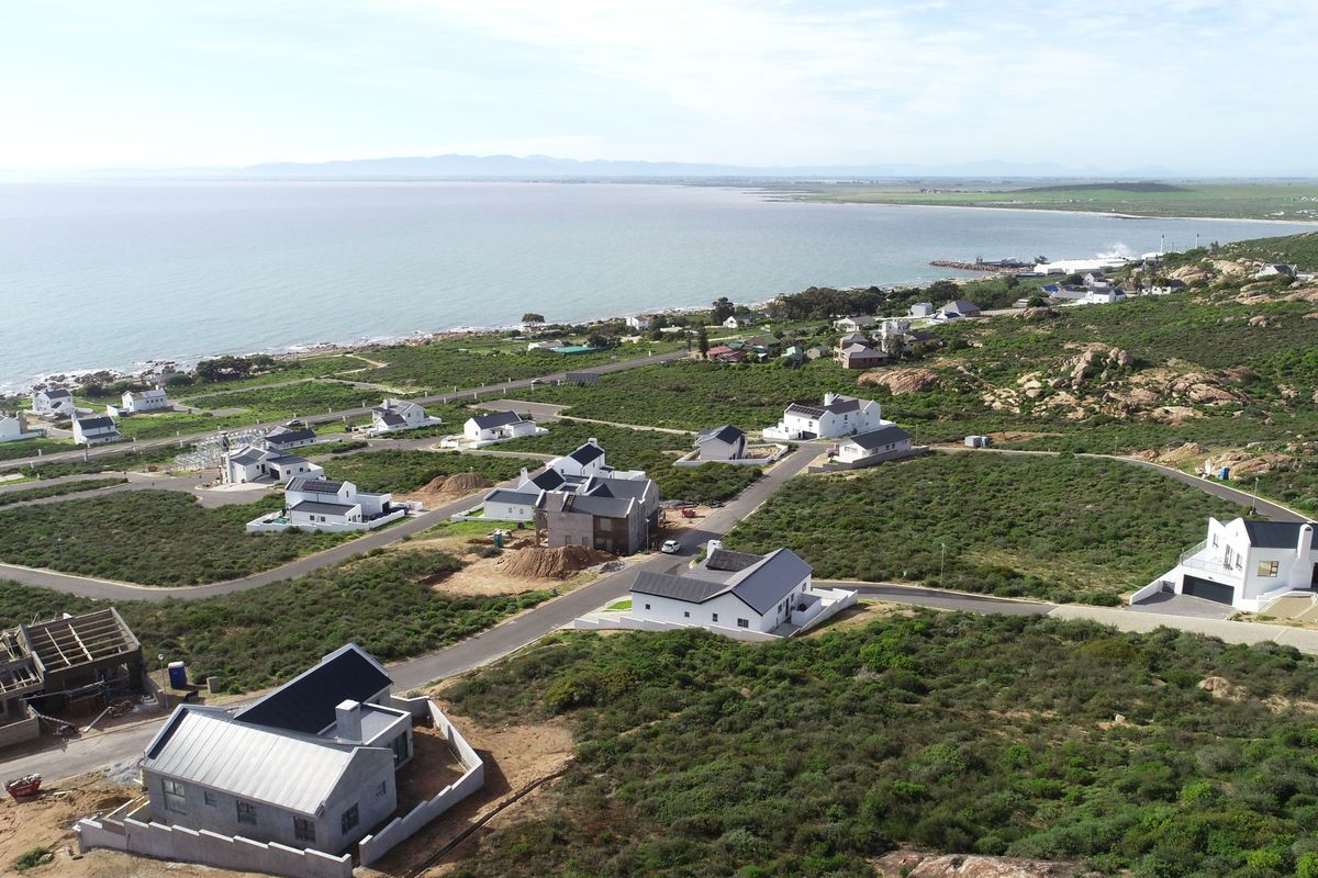 Aerial view of a coastal residential development featuring modern homes, paved infrastructure, and surrounding natural landscape with ocean views.