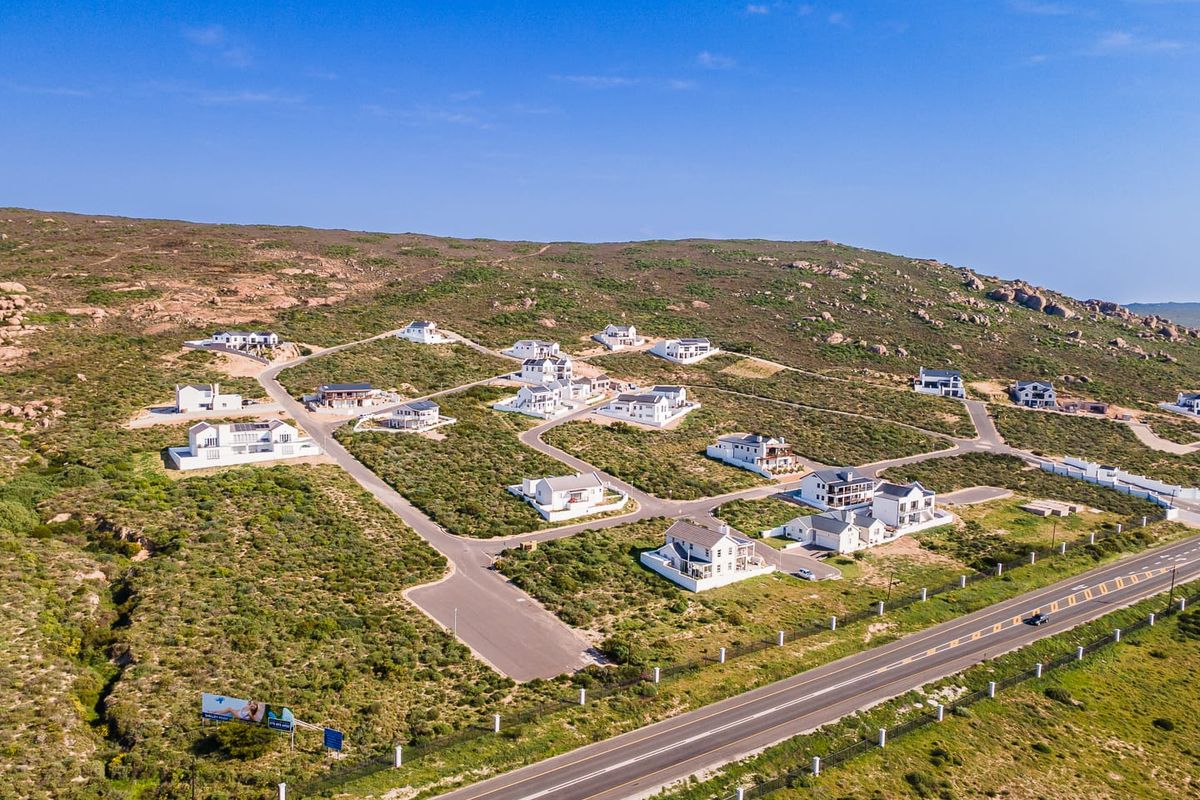 Aerial view of a residential estate development featuring multiple detached homes, paved internal roads, and surrounding natural landscape.
