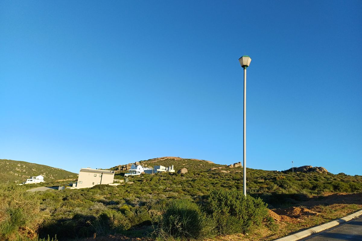 A view of the residential street approach featuring a street light, paved road edge, and natural landscape with distant hillside properties.