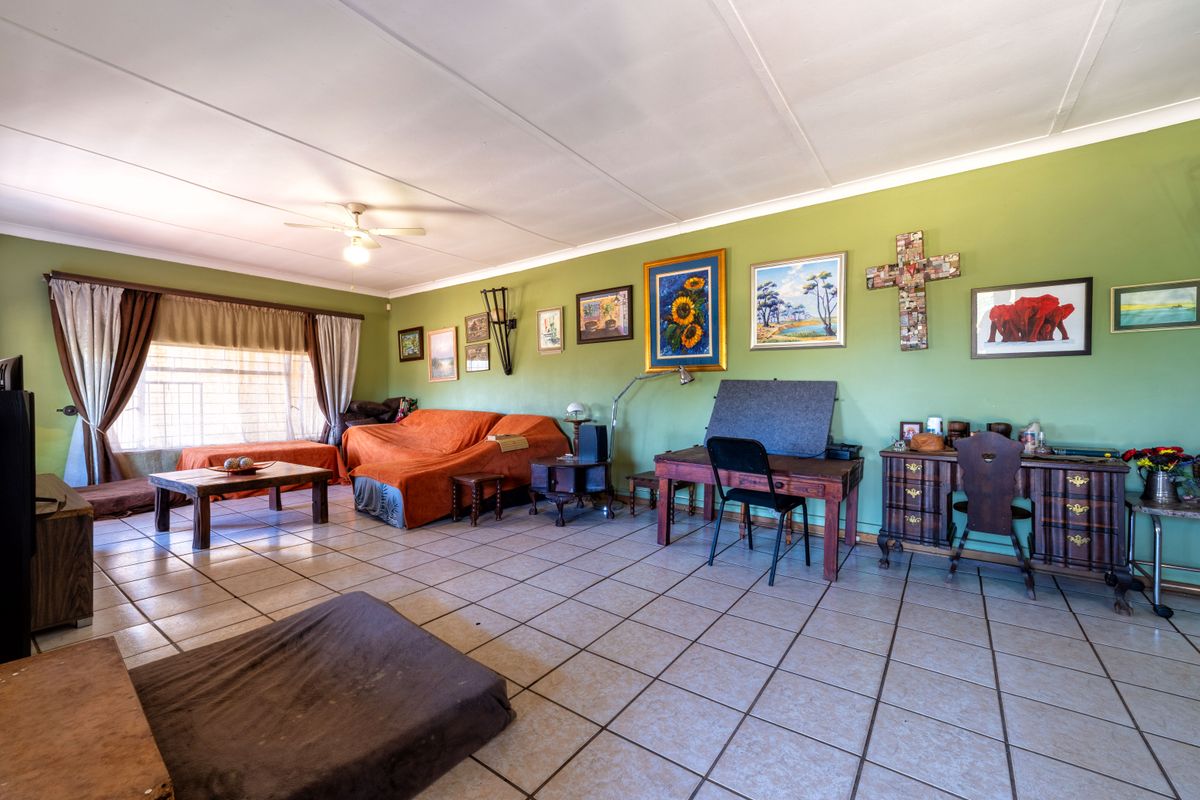 Spacious living room featuring tiled flooring, a ceiling fan, and large windows with security bars, offering a functional layout for family living.