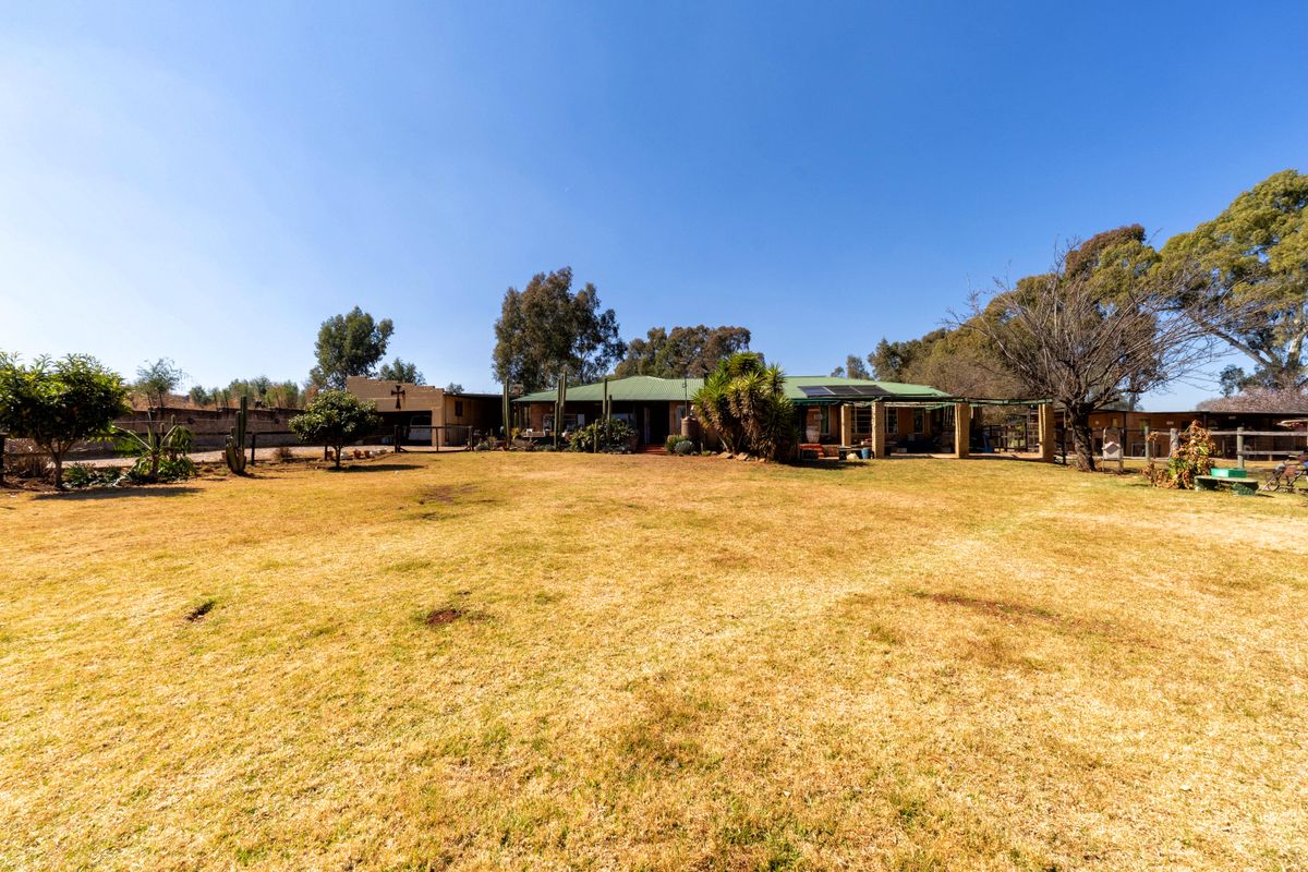A wide-angle view of the rear exterior of the small holding, featuring a large lawn, covered patio area, and established trees under a clear sky.