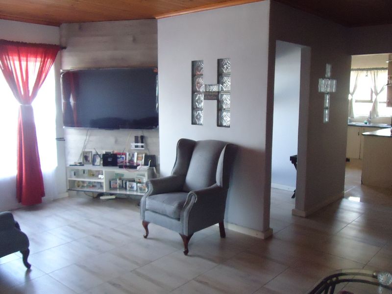 A living room featuring tiled flooring, a timber ceiling, and a decorative glass block feature wall, with an open flow to the adjacent kitchen area.