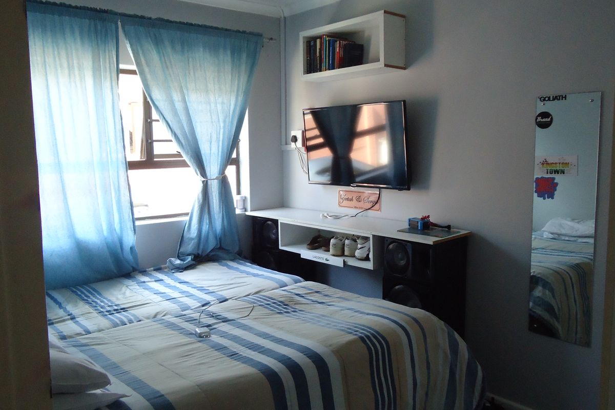 A functional bedroom featuring a wall-mounted media console, built-in shelving, and a window with security bars.