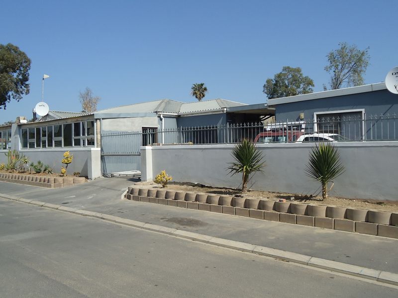 Front exterior view of the property featuring a perimeter wall with security fencing, a sliding gate, and a paved driveway area.