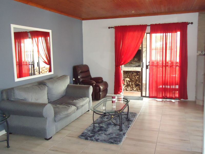 A living room featuring tiled flooring, a timber ceiling, and a sliding glass door providing access to an outdoor area with a built-in fireplace.