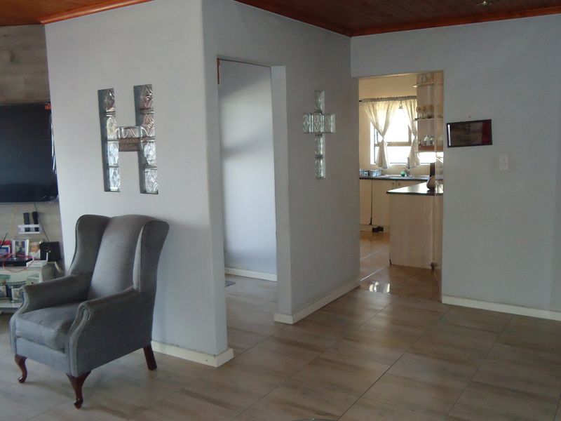 A living area featuring tiled flooring, a timber ceiling, and a glass block feature wall, with an open transition into the kitchen area.