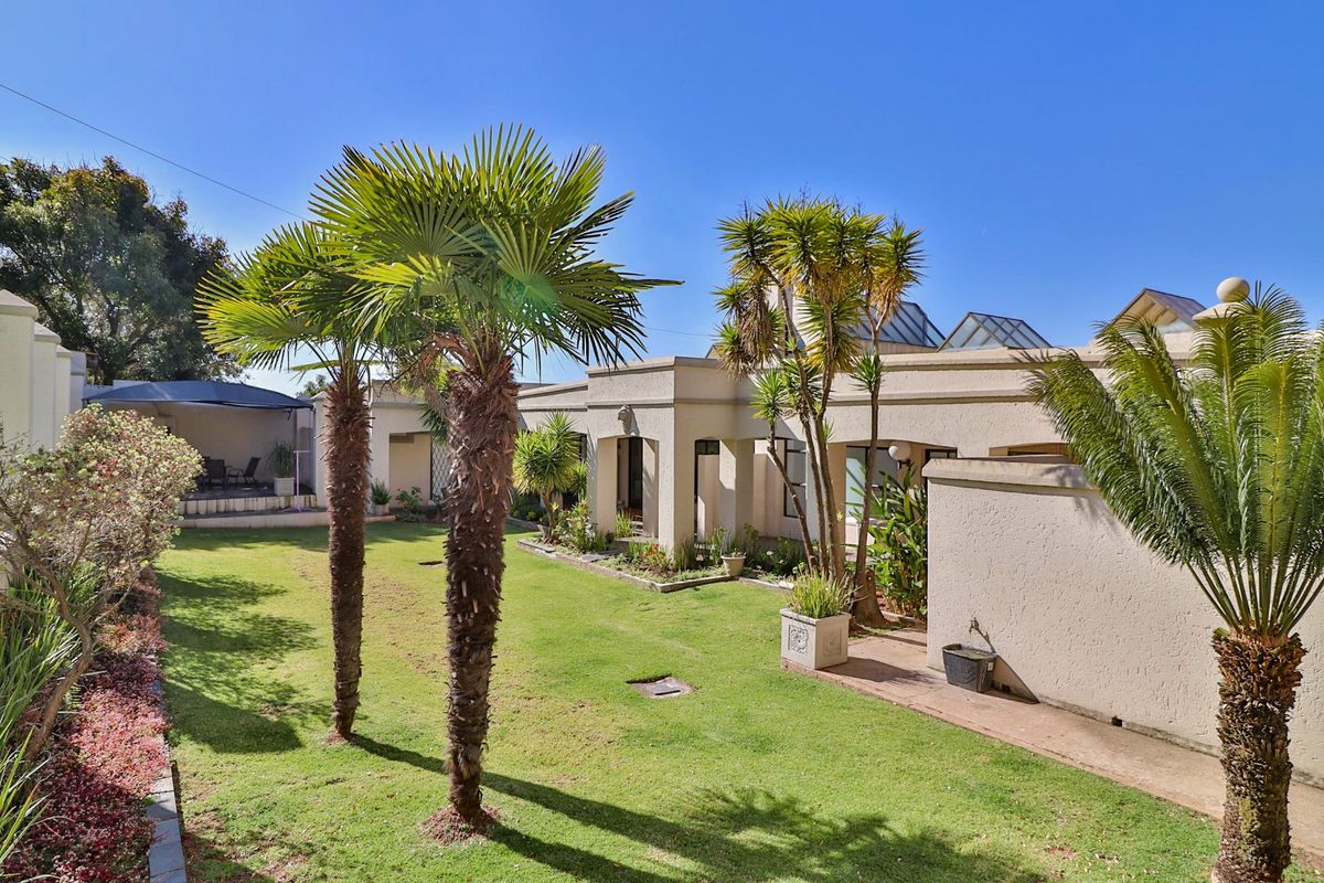 A well-maintained rear garden featuring a manicured lawn, mature palm trees, and a paved walkway leading to a covered patio area.