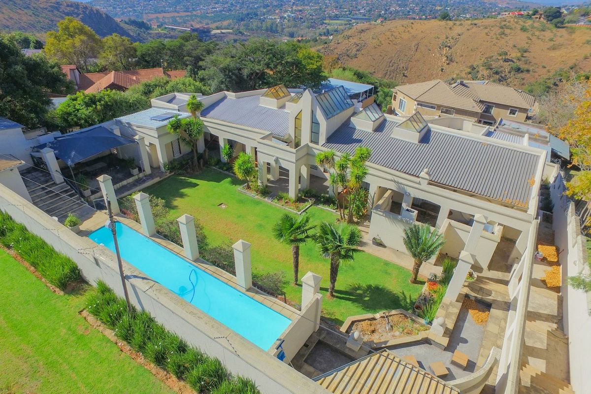 Aerial view of a modern residence featuring a swimming pool, landscaped garden, multiple skylights, and a spacious patio area set against a scenic hillside backdrop.