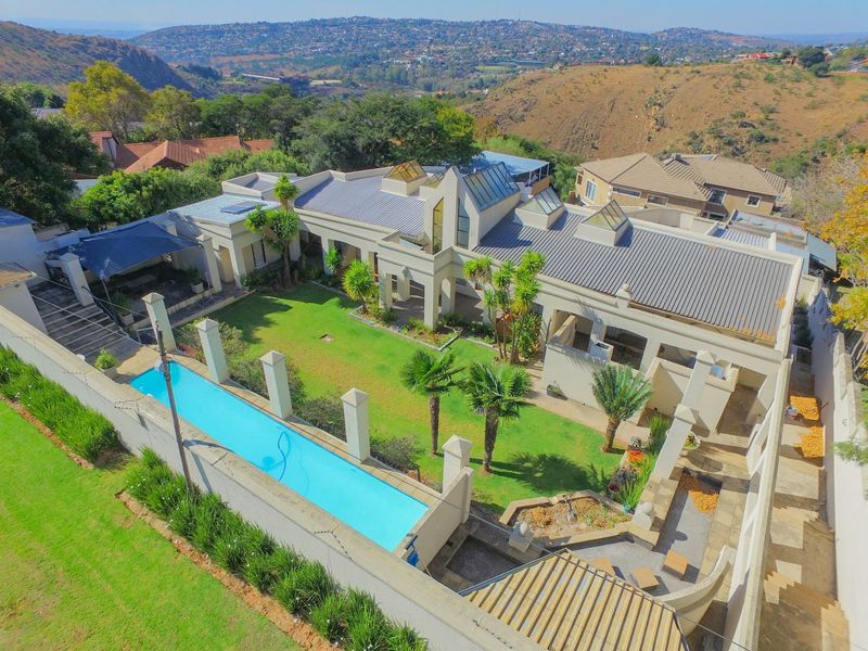 Aerial view of a modern residence featuring a swimming pool, landscaped garden, multiple skylights, and a spacious patio area set against a scenic hillside backdrop.