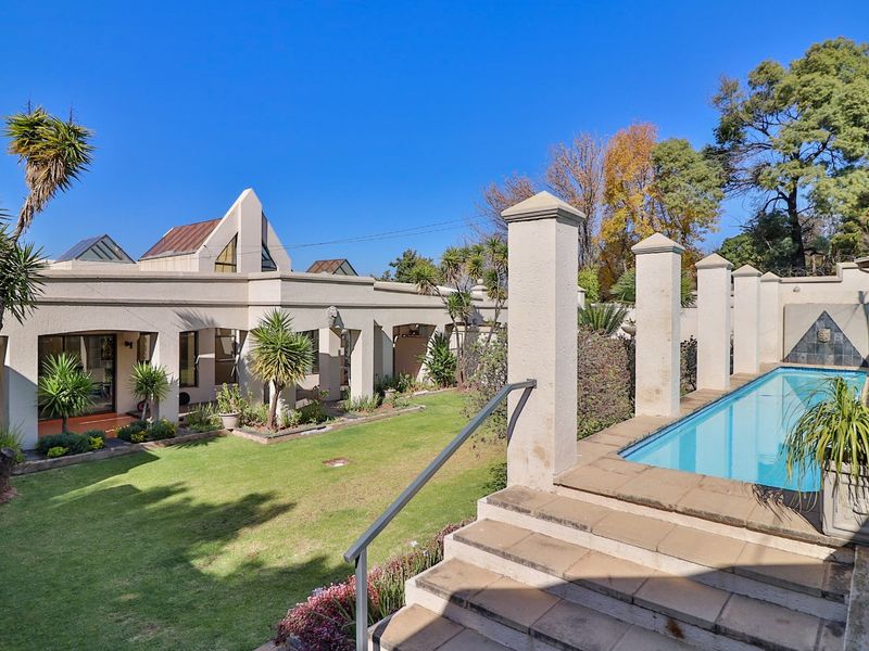 A well-maintained outdoor area featuring a swimming pool, stone pillars, and a landscaped garden with a paved staircase leading to the patio.