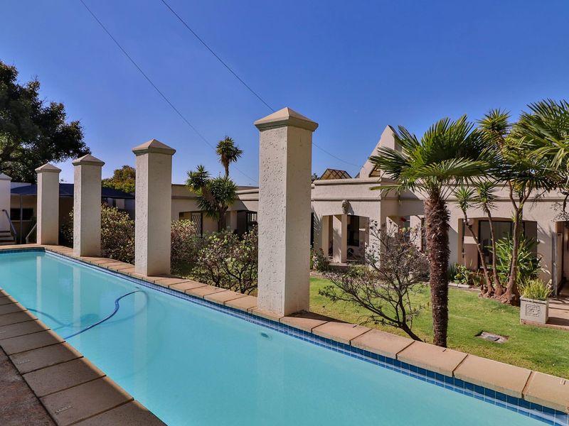 A well-maintained swimming pool area featuring stone coping, decorative concrete pillars, and a landscaped garden setting, perfect for outdoor relaxation.