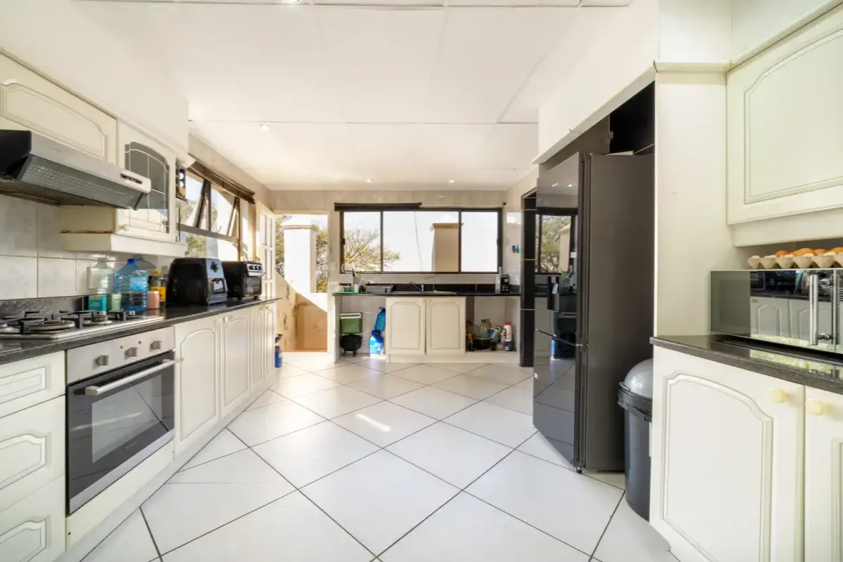 A functional kitchen featuring white cabinetry, a gas hob, built-in oven, and tiled flooring with direct access to an outdoor area.