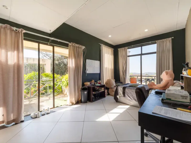 Spacious bedroom featuring large windows, tiled flooring, and sliding glass doors that provide direct access to an outdoor patio area.