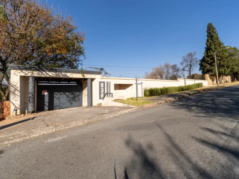 Street view of the property frontage featuring a secure boundary wall, electric fencing, and a private driveway entrance.