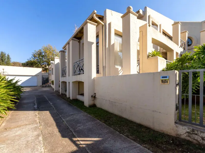 Front exterior view of the property featuring a concrete driveway, boundary wall with gate, and multi-level facade with balconies and garage access.